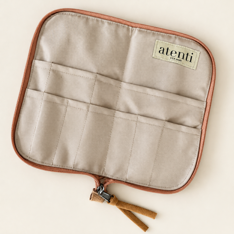 A square beige fabric organizer pouch with a rose gold zipper and brown leather tassel, featuring stitched compartments and a small 'alteni' brand label.